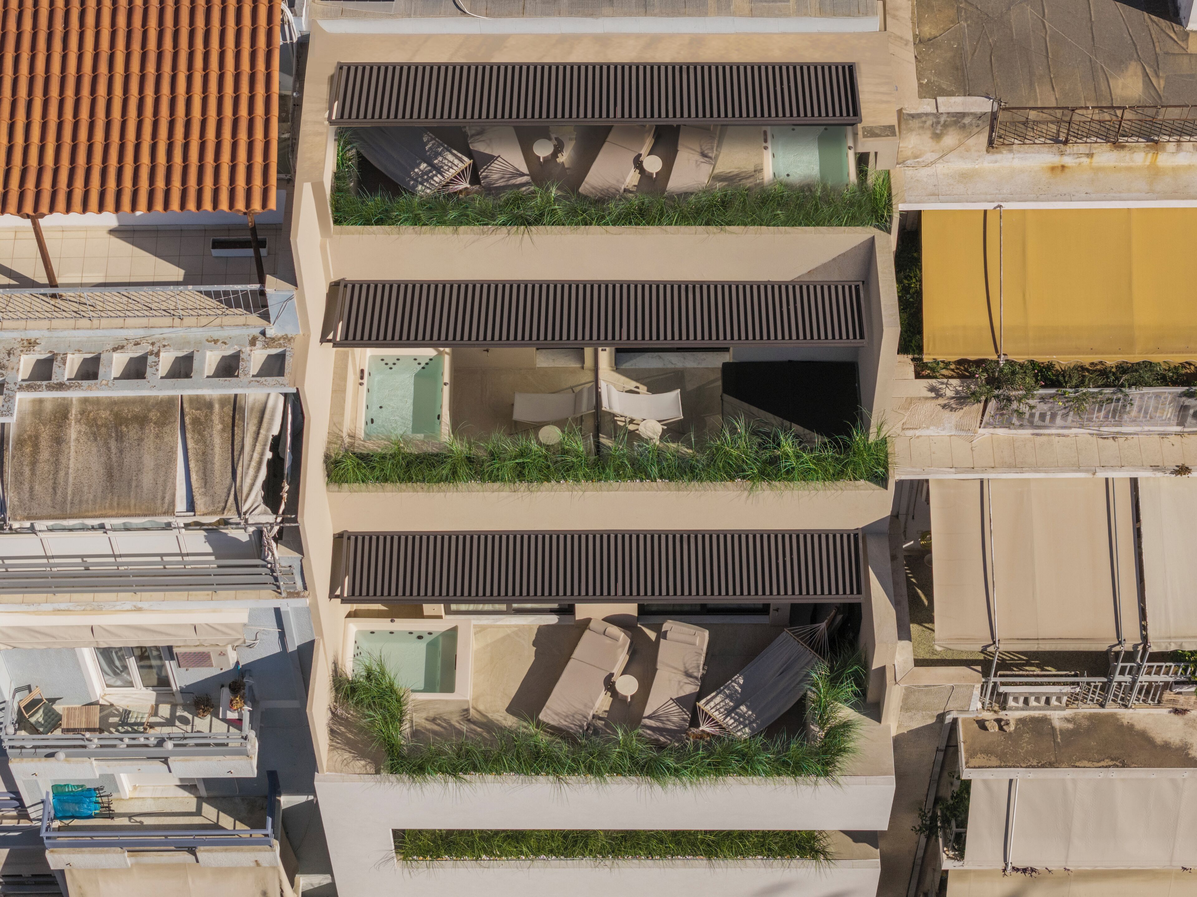 A modern building with multiple balconies, each with a small garden area and outdoor furniture.