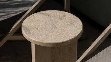 A round, textured table in a sunlit room with a sloped ceiling and a cushioned seating area.
