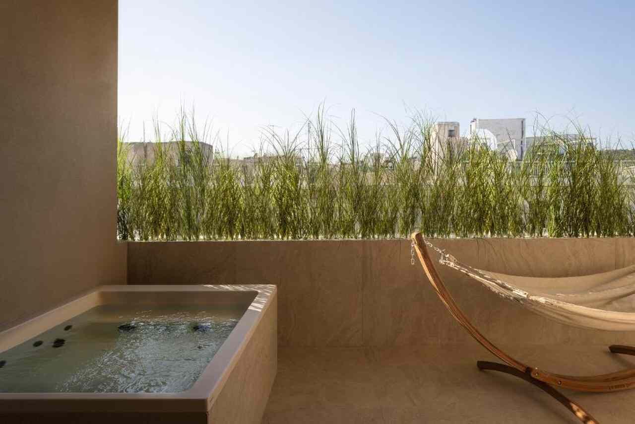 Una terraza en la azotea con jacuzzi, una hamaca y vistas a pastizales y edificios.