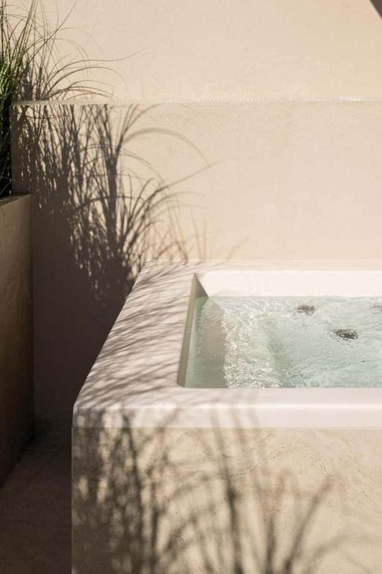 A spa area with a hot tub, surrounded by a concrete wall and a planter with greenery.
