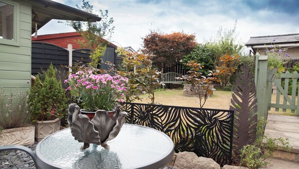 A patio area with a round glass table, potted plants, and a decorative metal fence. - Snug Corner (Holmfirth)
