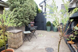 A patio with a table and chairs, surrounded by potted plants and a black gate.