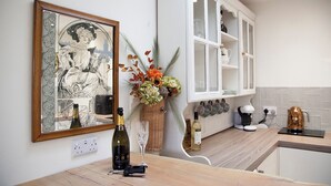 A kitchen with a large framed artwork, a bottle of wine, and a vase of flowers on the counter. - Snug Corner (Holmfirth)