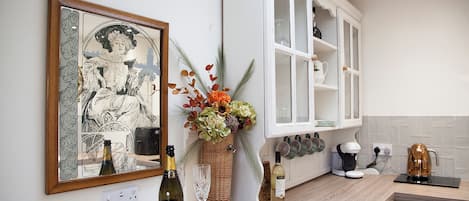 A kitchen with a large framed artwork, a bottle of wine, and a vase of flowers on the counter.