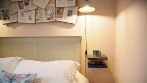A bedroom with a bed, a wall-mounted lamp, and a shelf with books and a mug. - Snug Corner (Holmfirth)