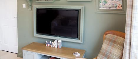 Una sala de estar con un televisor de pantalla plana, obras de arte enmarcadas, una mesita con figuritas y un sillón a cuadros.