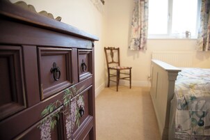 Un dormitorio con un aparador de madera, una silla, una cama con edredón floral y una ventana con cortinas.