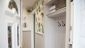 A hallway with white walls, a door with two hooks, a mirror, and a window with a stained glass design. - Snug Corner (Holmfirth)