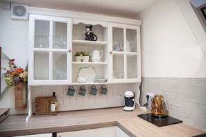 A kitchen with a white cabinet, a coffee maker, and a kettle on the counter. - Snug Corner (Holmfirth)