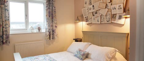 Une chambre à coucher avec un lit, une fenêtre avec des rideaux, un mur où sont accrochés des papiers et un radiateur.