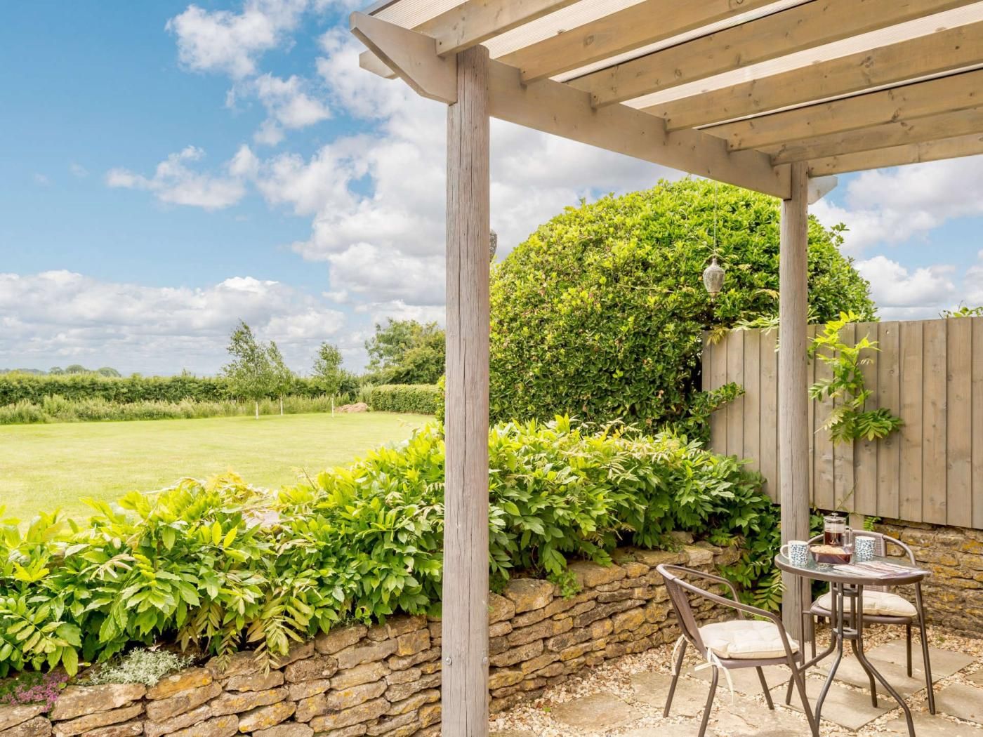 A covered patio area with stone walls, a wooden fence, and a table with chairs.