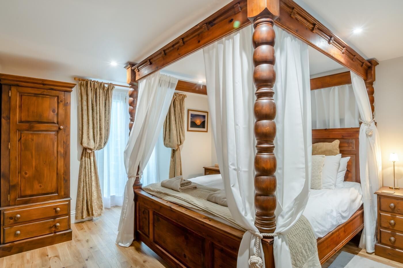 A four-poster canopy bed with a wooden headboard, a wooden nightstand with a lamp, and a wooden wardrobe.