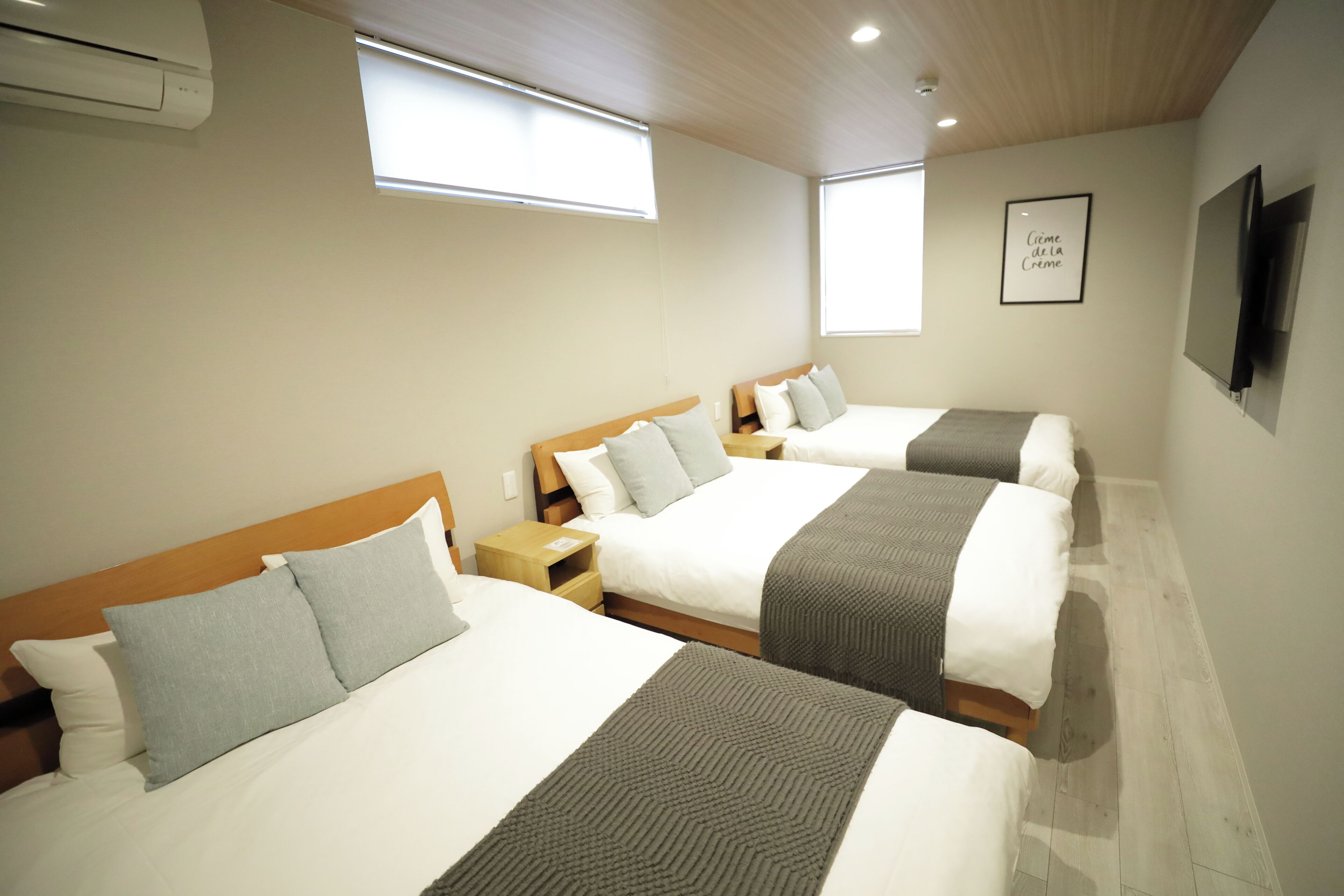 Une chambre d’hôtel avec trois lits, chacun doté d’une tête de lit en bois, d’une table de chevet et d’une petite table.