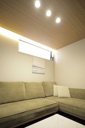 A room with a green sectional sofa, a white coffee table, recessed ceiling lights, and a wall-mounted artwork. - Koti Sopo Universal Bay 4 by Liaison (Minato ward)