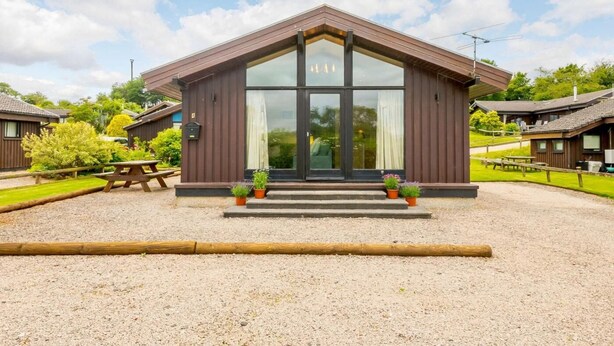 A lodge with a large entrance, outdoor seating, and a gravel driveway. - 3 Bed in Penrith (oc-88212) (Yanwath)