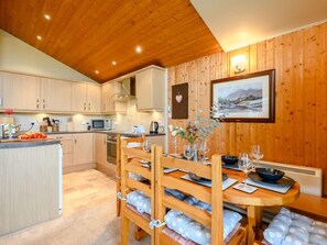 A cozy kitchen with wooden cabinets, a dining table set for four, and a framed landscape painting on the wall.