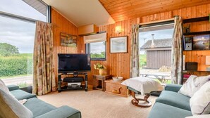 A cozy living room with a television, wooden walls, and a large window. - 3 Bed in Penrith (oc-88212) (Yanwath)