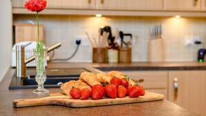 A kitchen counter with croissants and strawberries, a vase with a red flower, and a knife block in the background. - 3 Bed in Penrith (oc-88212) (Yanwath)