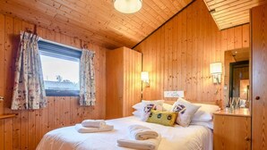A wooden-paneled bedroom with a bed, two wall-mounted lamps, a bedside table with a lamp, and a mirror. - 3 Bed in Penrith (oc-88212) (Yanwath)