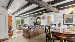 Ein geräumiger Wohnbereich mit Holzbalkendecke, einer Couch, einem Esstisch mit Stühlen und einem Kamin.
