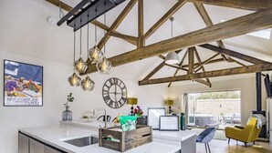 A modern kitchen with a large island, wooden beams, hanging pendant lights, and a view to the outside. - 2 Bed in Driffield (oc-88238) (Lund)