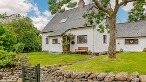 Ein weißes Haus mit Steinmauer, einem Holztor und einem großen Baum im Garten.