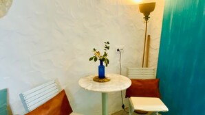 Ett litet rum med en vit vägg, ett runt bord med en blå vas, två vita stolar med bruna kuddar och en hög golvlampa.