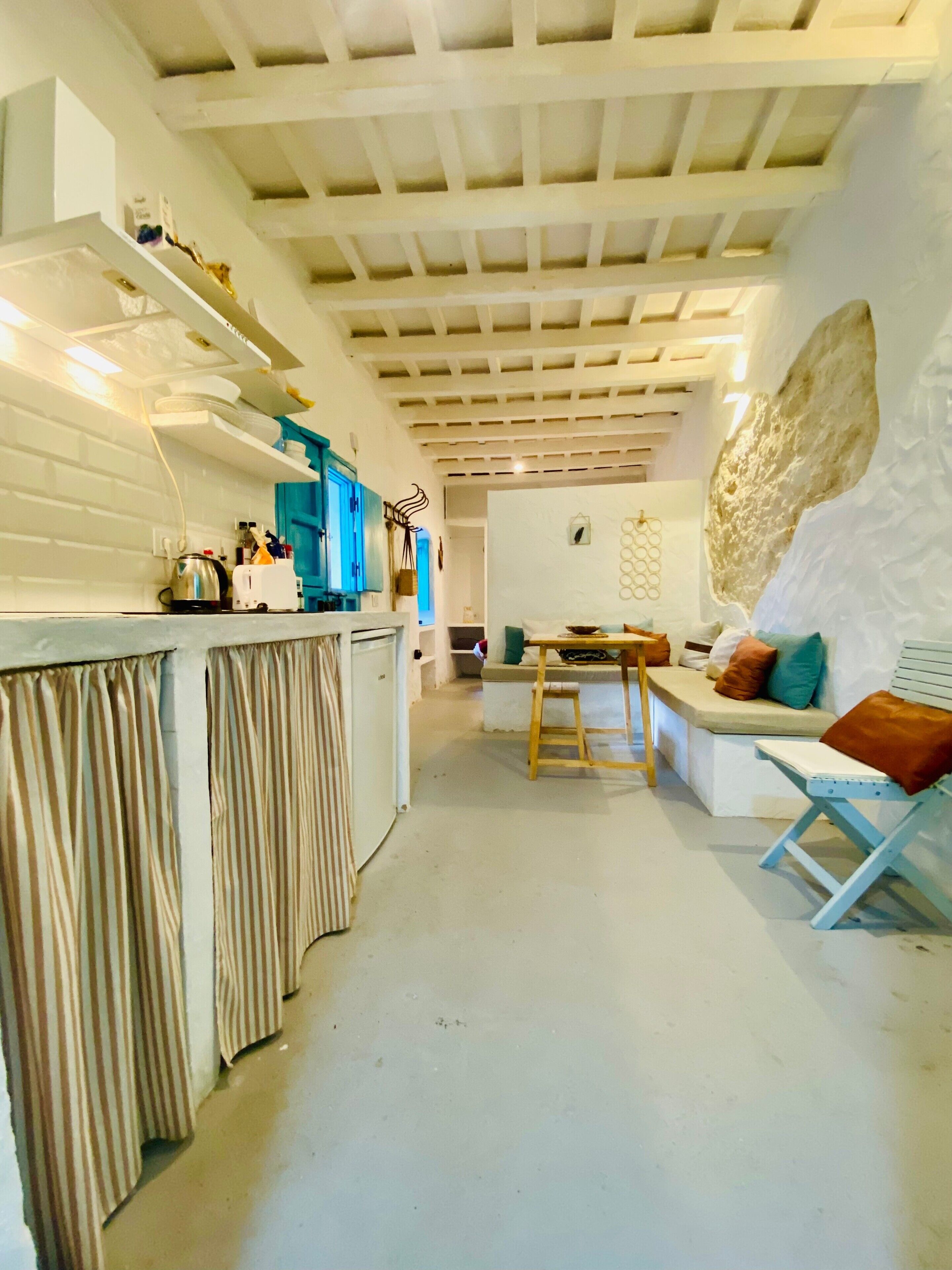 Une cuisine moderne avec un plafond blanc, un coin repas doté d’une table en bois et un espace détente avec un canapé et des coussins.