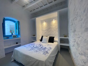 A bedroom with a bed, a window, and built-in shelves. - Cave apartment in the heart of the center (Vejer de la Frontera)