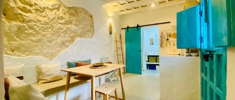 A cozy room with a stone wall, a wooden table, a bench, and a teal door.