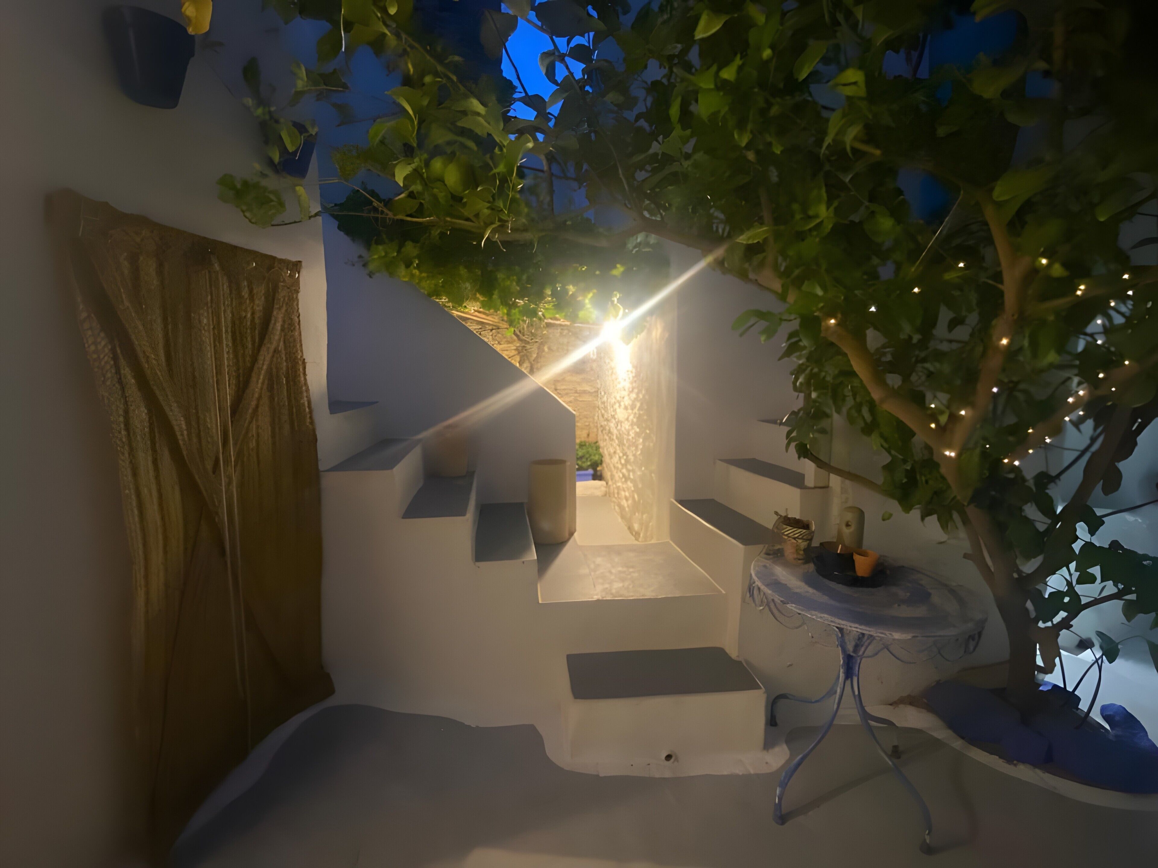 Un espace extérieur moderne comprenant un escalier, une petite table et un arbre décoré de guirlandes lumineuses.