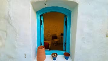 Een raam met een blauw kader, een witte muur en een klein schap met een terracotta pot en twee blauwe kommen.