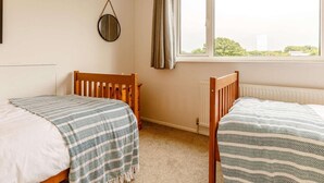 Quarto com duas camas de madeira, um radiador, uma janela com cortinas e um espelho redondo na parede.