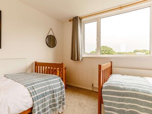 Ein Schlafzimmer mit zwei Holzbetten, einem Heizkörper, einem Fenster mit Vorhängen und einem runden Spiegel an der Wand.