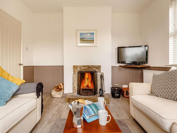 A living room with a fireplace, a television, and a coffee table with a book and mug. - 3 Bed in Truro (oc-88404) (Rose)