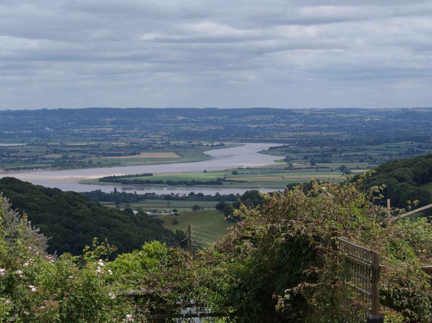 A river winding through a valley with a fence in the foreground.