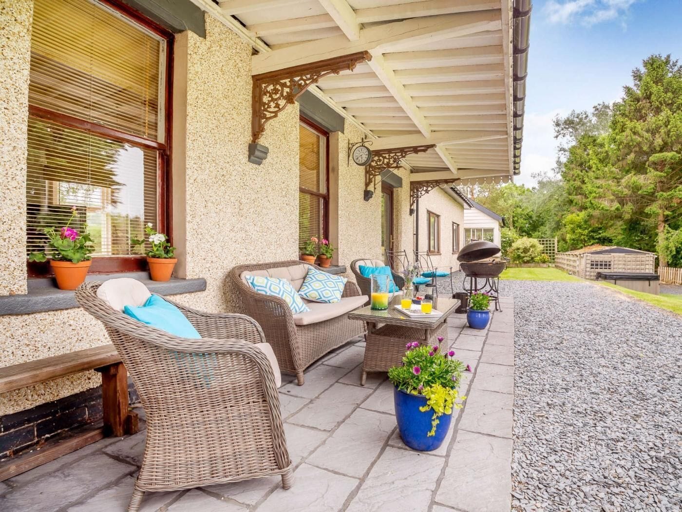 A covered patio with wicker furniture, potted plants, and a barbecue grill.