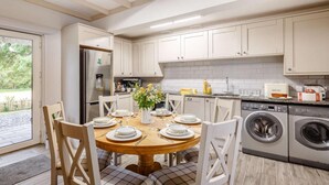 A modern kitchen with white cabinets, a built-in oven, a washing machine, and a dining area with a round table and chairs. - 3 Bed in Bala (oc-88351) (Fron-goch)