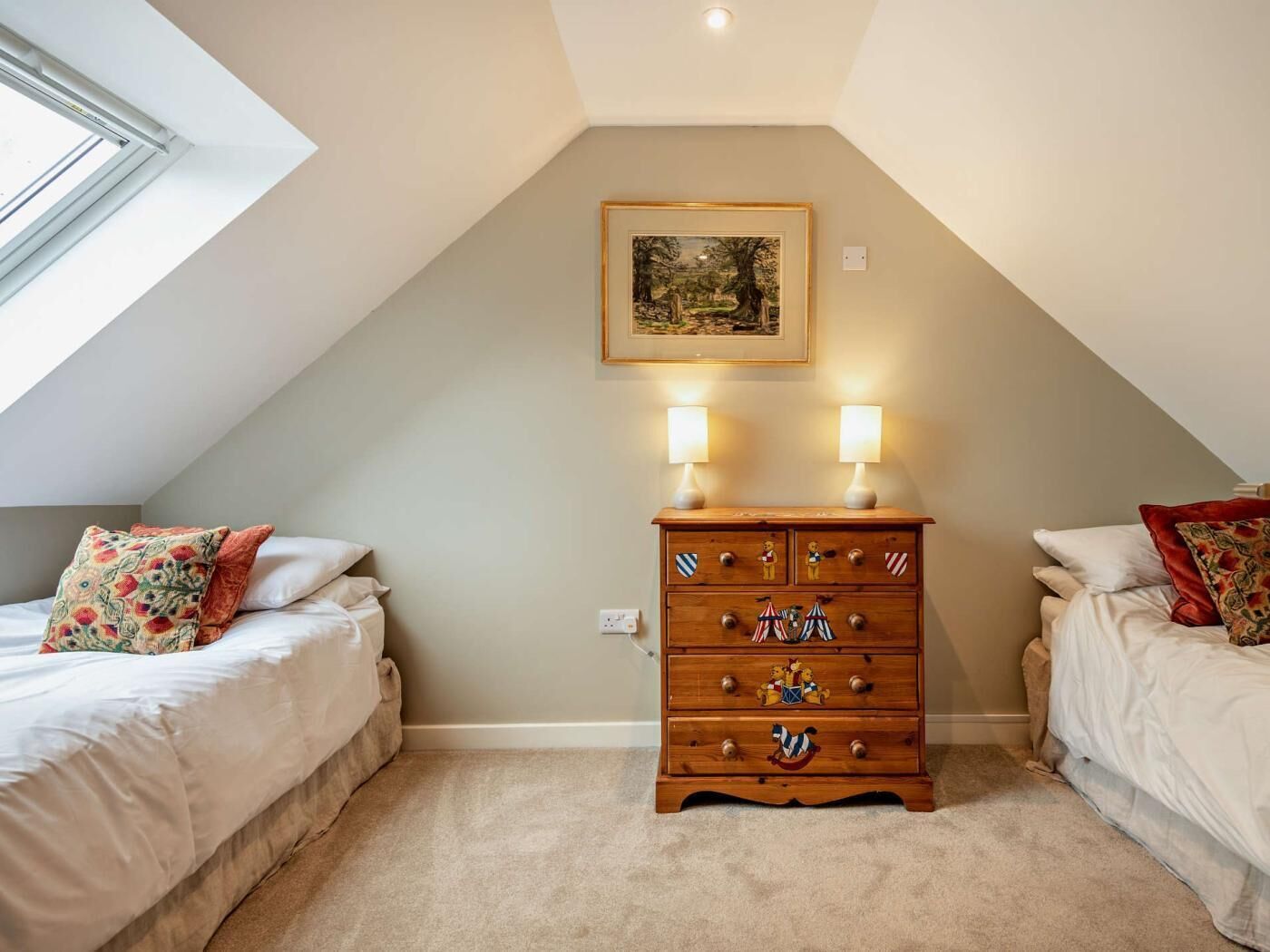 A bedroom with two beds, a wooden dresser, a painting on the wall, and a skylight.