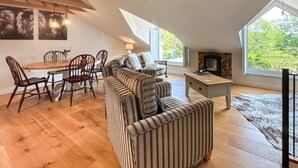 Uma sala de estar estilo loft com área de jantar, vigas de madeira, lareira e janelas amplas.