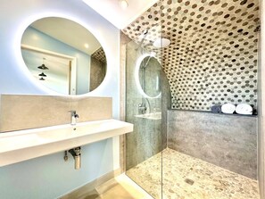 Un baño moderno con un espejo redondo, un lavamanos y una ducha con un patrón hexagonal distintivo en las paredes.