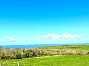 A coastal landscape with rolling green fields, a clear blue sky, and the sea in the distance.