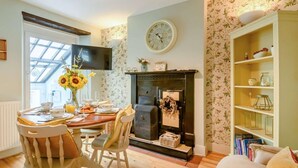 Ein gemütliches Wohnzimmer mit Kamin, ein Essbereich mit Tisch für Zwei und eine Bücherwand voller Bücher.