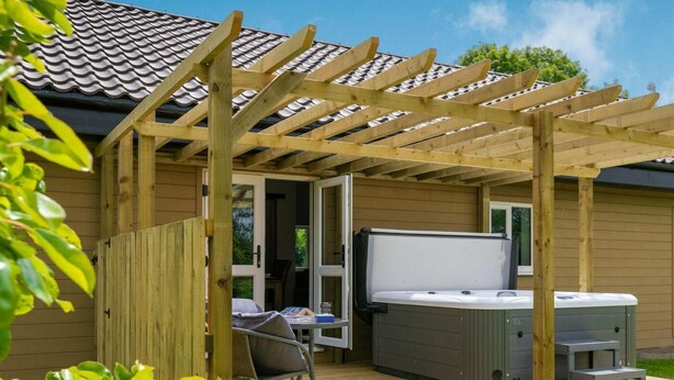 Un patio techado con jacuzzi, pérgola de madera y una pequeña mesa con sillas.