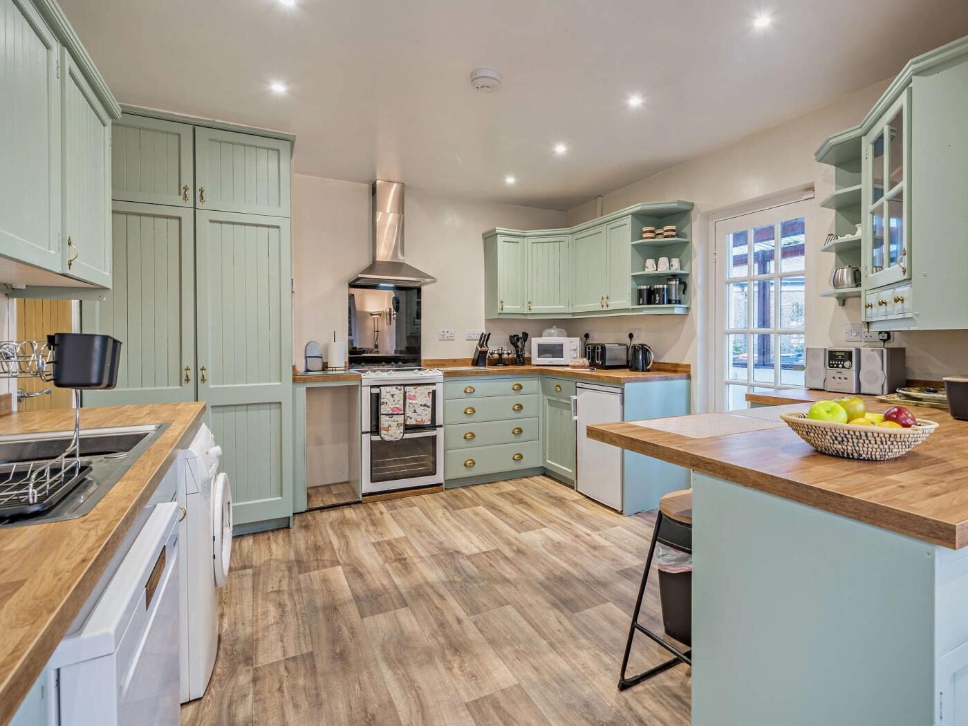 A modern kitchen with light green cabinets, a stainless steel range hood, and a wooden countertop.