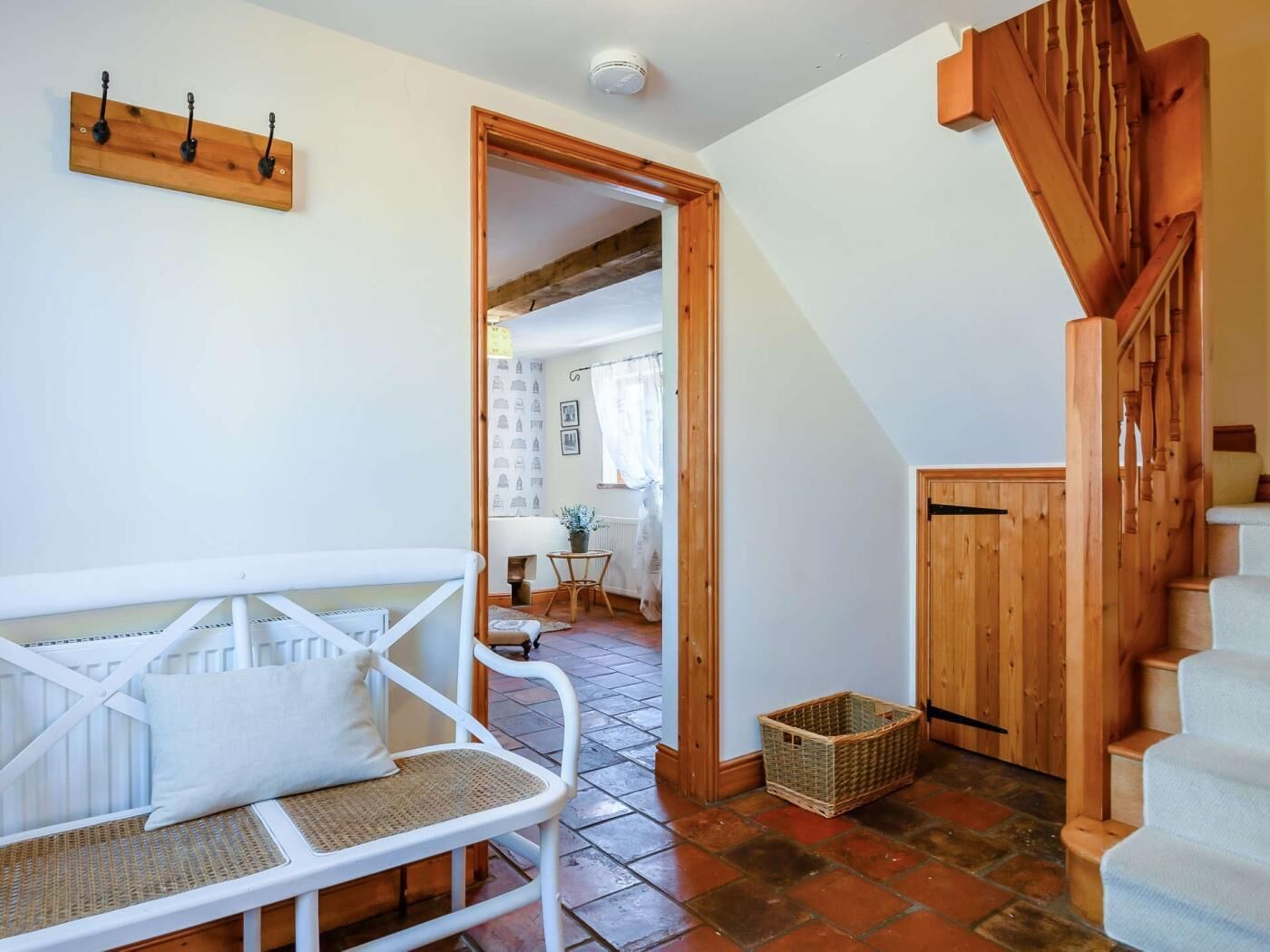 A room with a white chair, a wooden staircase, and a doorway leading to another room.