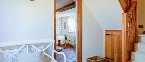 A room with a white chair, a wooden staircase, and a doorway leading to another room.