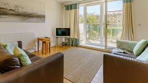 A living room with a sofa, a TV, a small table, and a sliding glass door leading to a balcony. - 2 Bed in Tenby (oc-88738) (Tenby)