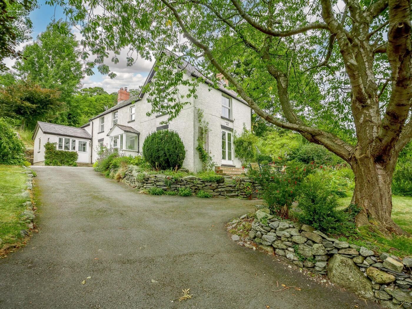 A white house with a stone wall and a driveway leading to the entrance.