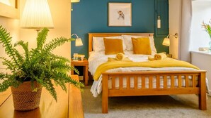 Ein Schlafzimmer mit einem hölzernen Bett, einem Blumentopf mit einem Farn, einer Nachttischlampe und einem gerahmten Bild an der Wand.